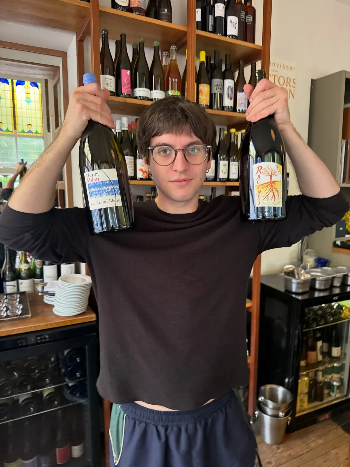 a colleague holding up two bottles in front of the wine wall